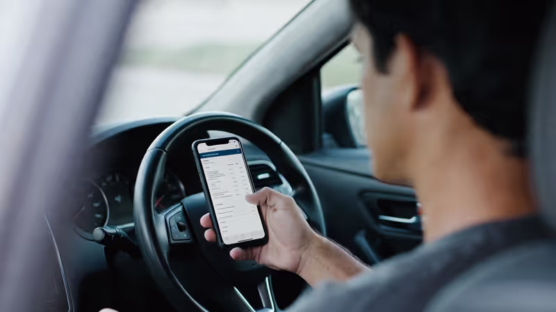 Driver looking at an insurance policy summary on a phone inside a parked car.